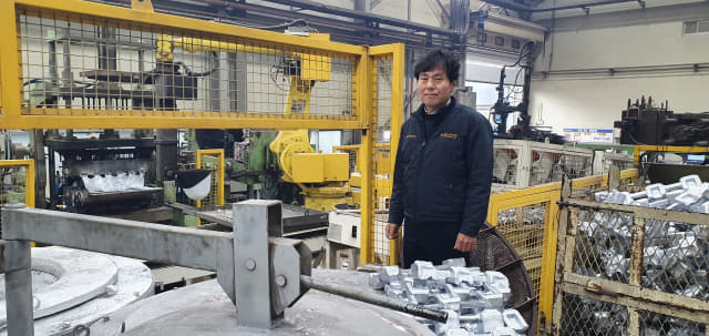 김해 나우산업 권용영 대표가 주조자동화 로봇 옆에서 포즈를 취하고 있다.