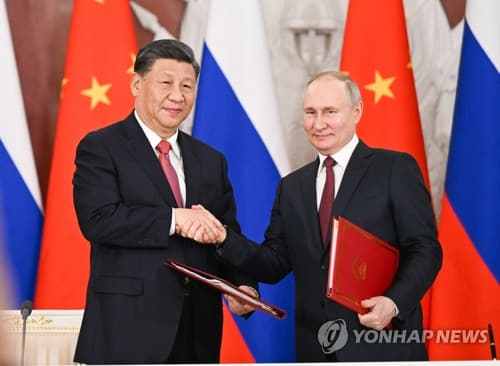 【モスクワ新華社＝聯合ニュース】中国の習近平国家主席（左）とロシアのウラジーミル・プーチン大統領が２１日（現地時間）、ロシア・モスクワのクレムリン宮殿での首脳会談後、共同声明に署名し握手している。 そこには 