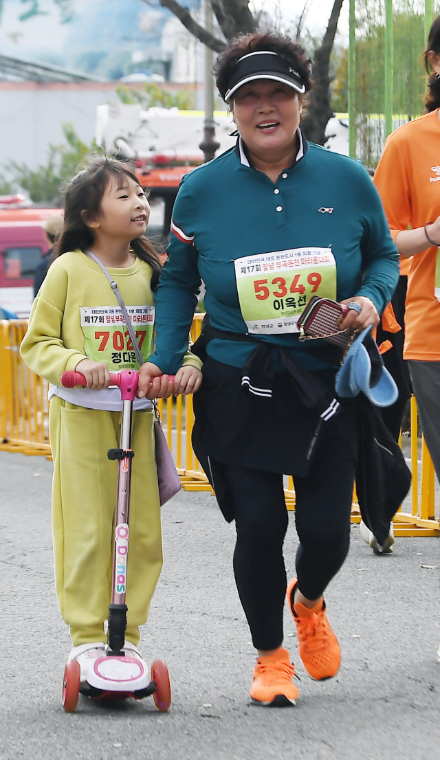 한 참가자가 킥보드를 탄 어린이와 함께 결승선을 향해 달리고 있다.