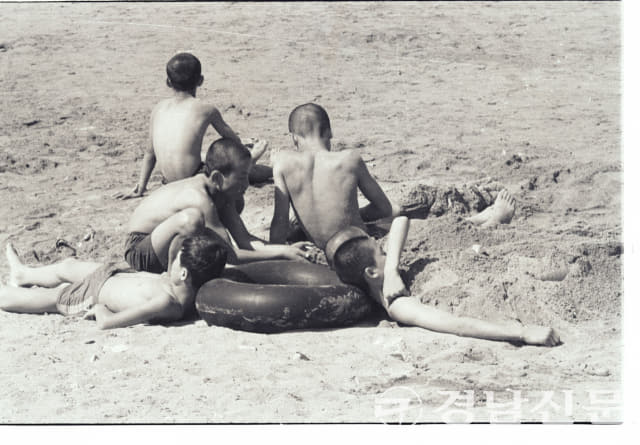1960년대 후반 추정 가포 해수욕장에서 검은 고무 튜브를 베고 모래찜질을 즐기는 소년들의 모습