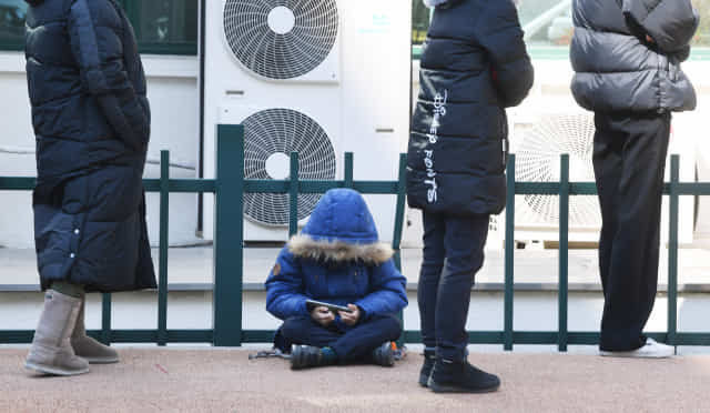 24일 오후 창원시 마산보건소 코로나19 선별진료소에서 바닥에 앉은 한 어린이가 스마트폰을 보며 검사를 기다리고 있다./김승권 기자/