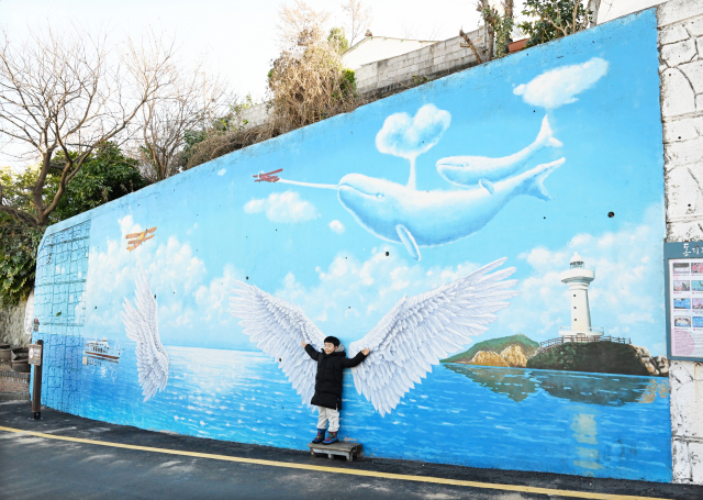 한 아이가 통영바다를 품은 날개 벽화 앞에서 포즈를 취하고 있다